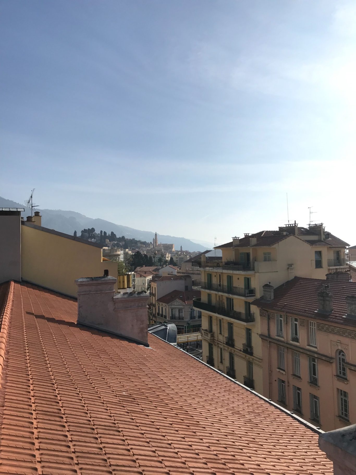 Vue d'un paysage urbain avec maisons et collines sous un ciel ensoleillé.